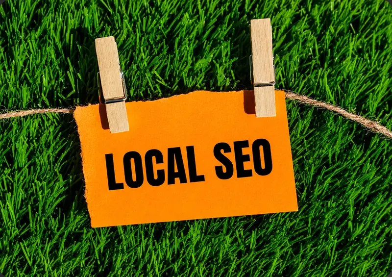 Étiquette orange LOCAL SEO accrochée par deux pinces à linge en bois sur une ficelle, devant un fond de gazon vert